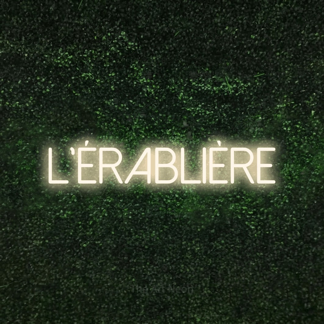 “L'érablière” LED neon sign in warm white, with thin sans-serif lettering, shown against a textured green hedge.