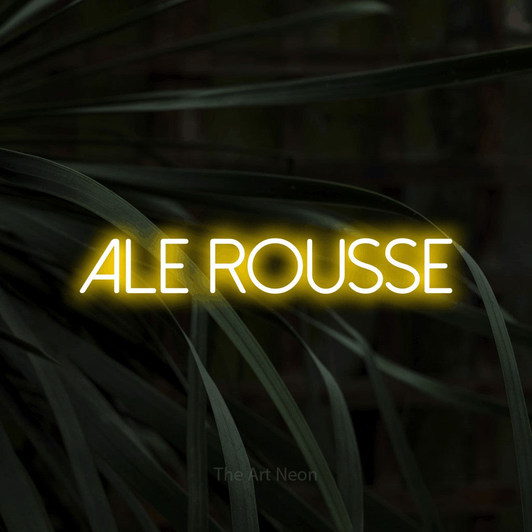 “Ale rousse” LED neon sign in yellow, with thin sans-serif lettering, shown against a close-up of dark foliage.