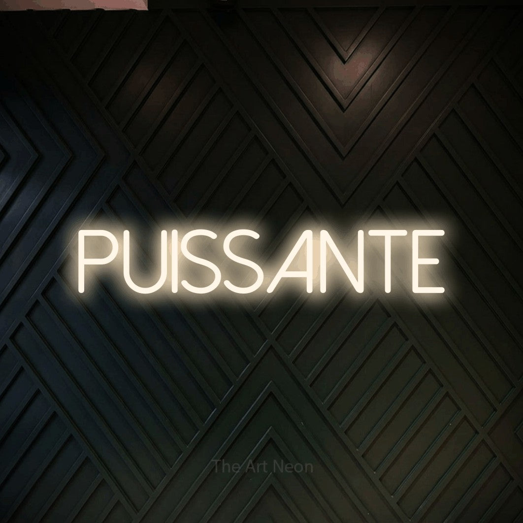 “Puissante” LED neon sign in warm white, with thin sans-serif lettering, shown against a black chevron-patterned wood wall.