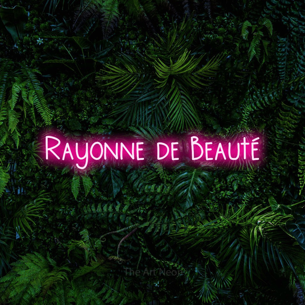 Enseigne néon LED « Rayonne de beauté » en rose vif, en lettres étroites dessinées à la main, présentée devant un feuillage tropical dense, pour un salon de beauté.