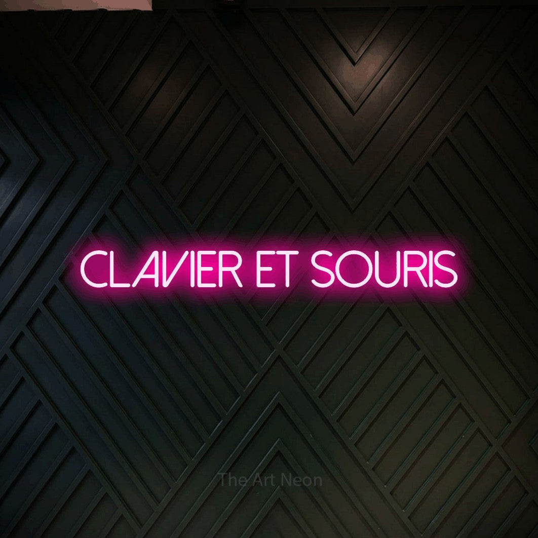 “Clavier et souris” LED neon sign in hot pink, with thin sans-serif lettering, shown against a black chevron-patterned wood wall.
