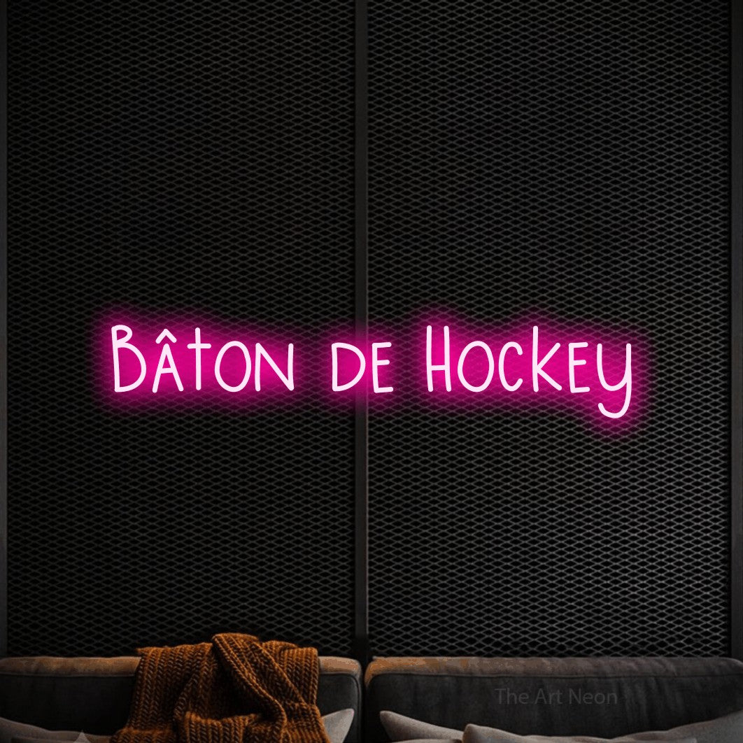 “Bâton de hockey” LED neon sign in hot pink, with narrow hand-drawn lettering, shown against a modern dark-toned seating area.