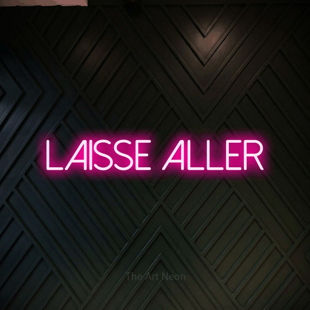 “Laisse aller” LED neon sign in hot pink, with thin sans-serif lettering, shown against a black chevron-patterned wood wall.