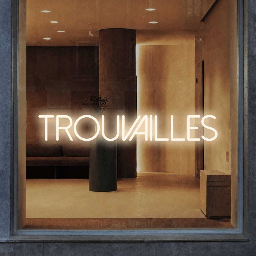 “Trouvailles” LED neon sign in warm white, with thin sans-serif lettering, shown against a warm-toned interior.