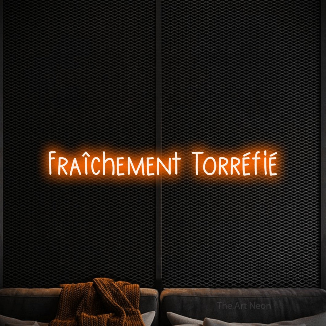 “Fraîchement torréfié” LED neon sign in orange, with narrow hand-drawn lettering, shown against a modern dark-toned seating area.