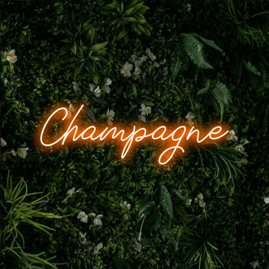 Néon LED « Champagne » en orange, en lettrage cursif, mis en scène sur un mur végétal vert et dense, pour un bar à la maison.