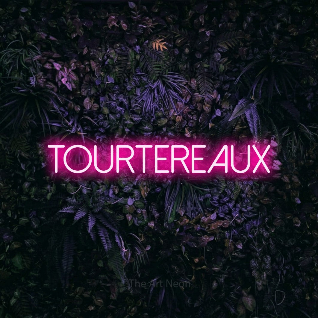 “Tourtereaux” LED neon sign in hot pink, with thin sans-serif lettering, shown against a dark wall with purple flowers.