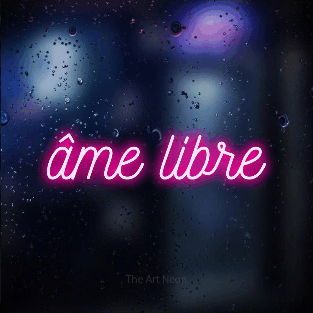 “Âme libre” LED neon sign in hot pink, with ornate cursive lettering, shown against glass with blue and purple reflections.