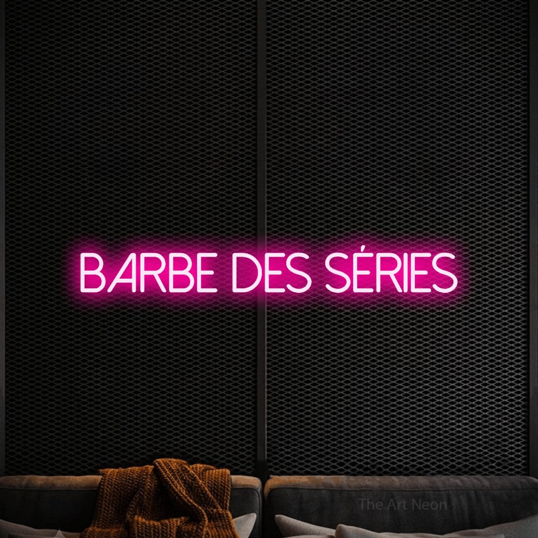 “Barbe des séries” LED neon sign in hot pink, with thin sans-serif lettering, shown against a modern dark-toned seating area.