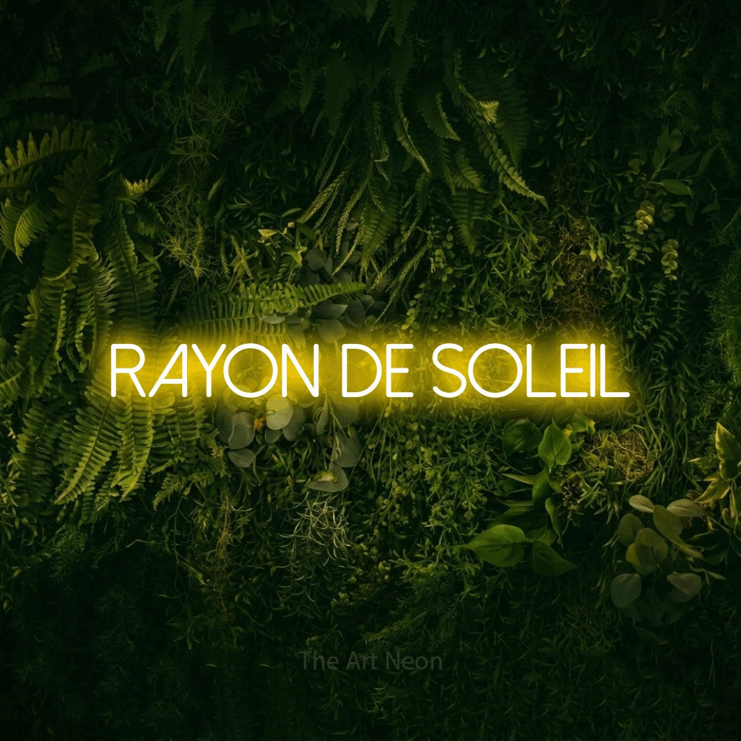 “Rayon de soleil” LED neon sign in yellow, with thin sans-serif lettering, shown against a dark moss and forest backdrop.