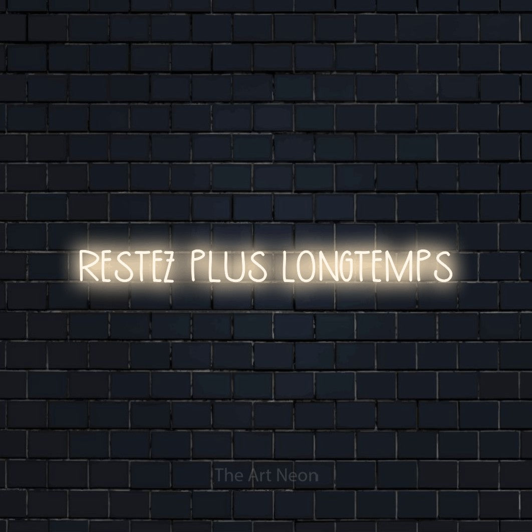 “Restez plus longtemps” LED neon sign in warm white, with narrow hand-drawn lettering, shown against a dark navy brick wall.