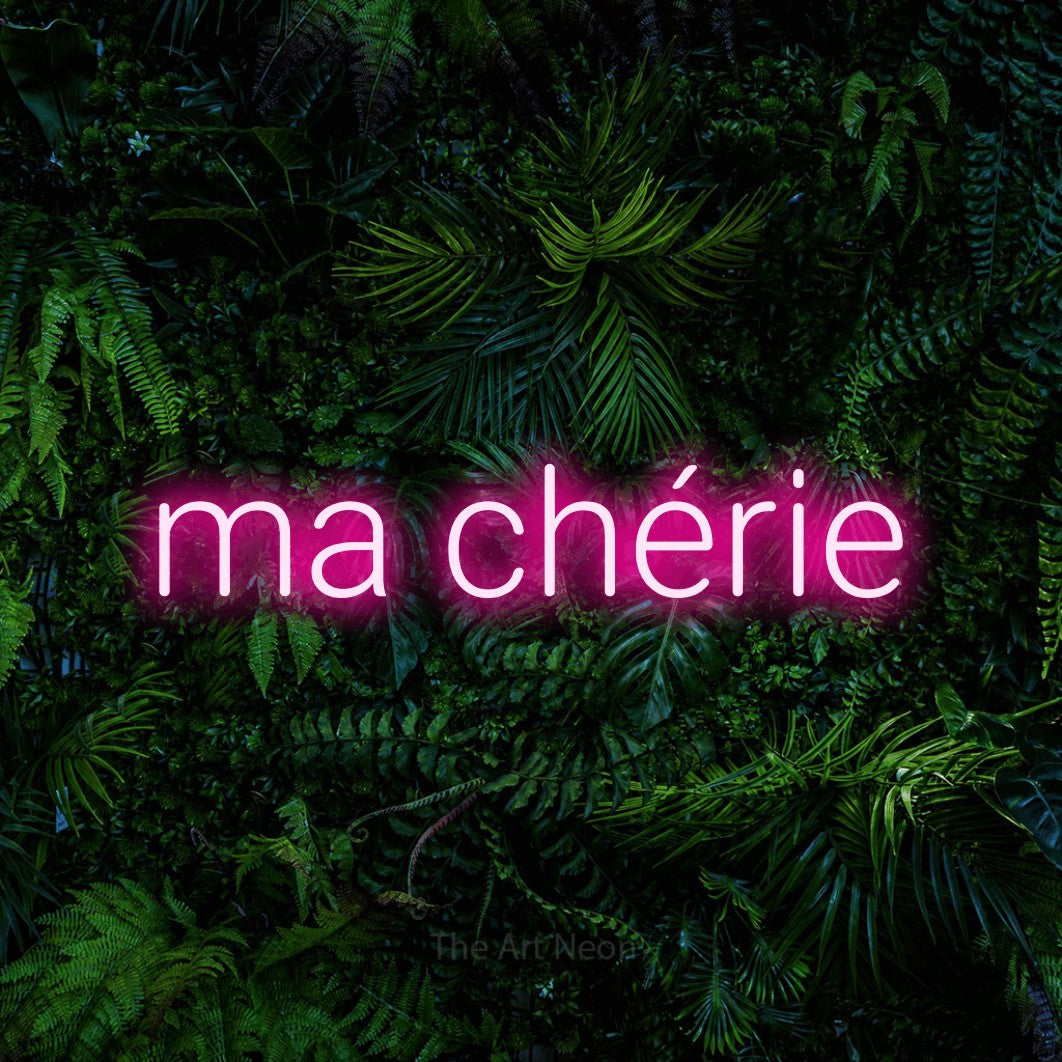 “Ma chérie” LED neon sign in hot pink, with rounded sans-serif lettering, shown against dense tropical foliage.