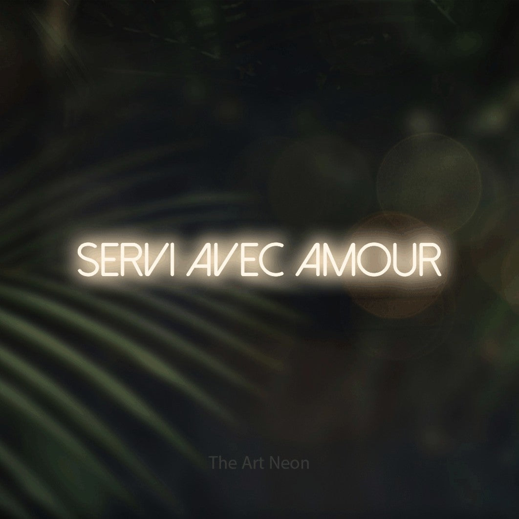 “Servi avec amour” LED neon sign in warm white, with thin sans-serif lettering, shown against a blurred palm and bokeh-light backdrop.