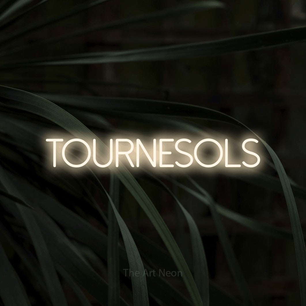 “Tournesols” LED neon sign in warm white, with thin sans-serif lettering, shown against a close-up of dark foliage.