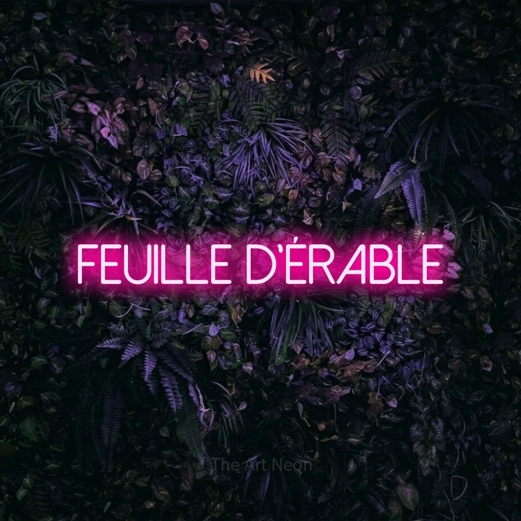 “Feuille d'érable” LED neon sign in hot pink, with thin sans-serif lettering, shown against a dark wall with purple flowers.