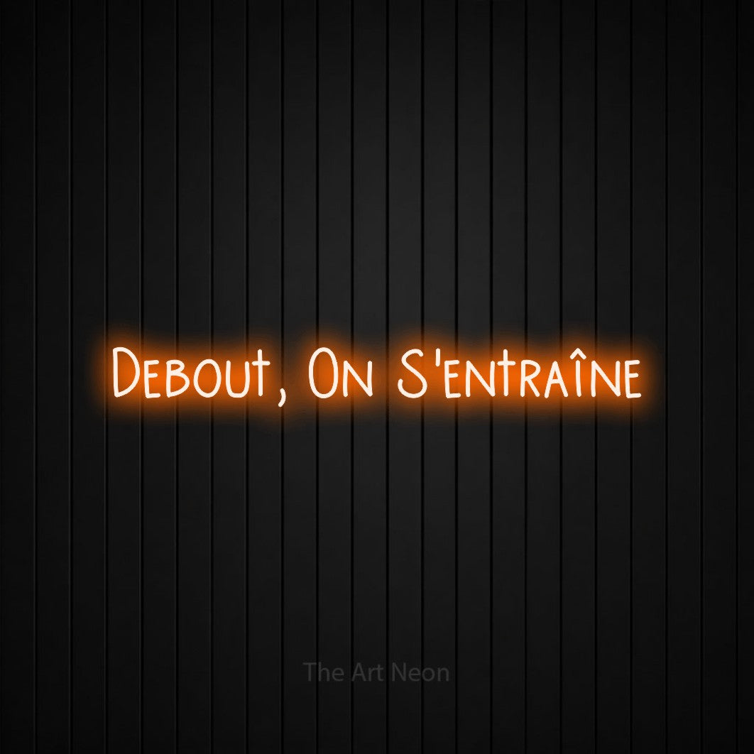 Néon LED « Debout, on s'entraîne » en orange, en lettres étroites dessinées à la main, mis en scène sur un mur de lattes verticales noires, pour un espace d’entraînement.
