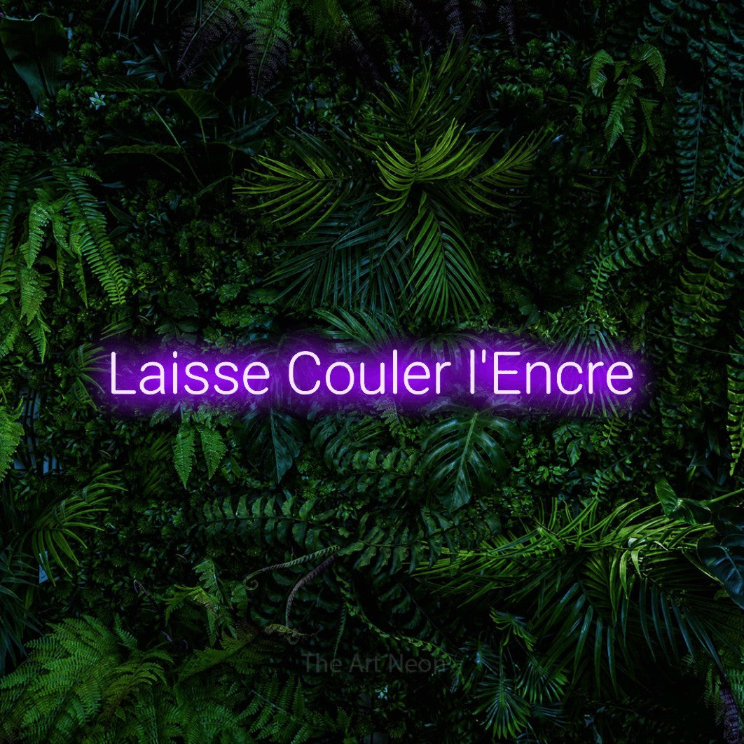 “Laisse couler l'encre” LED neon sign in purple, with rounded sans-serif lettering, shown against dense tropical foliage.