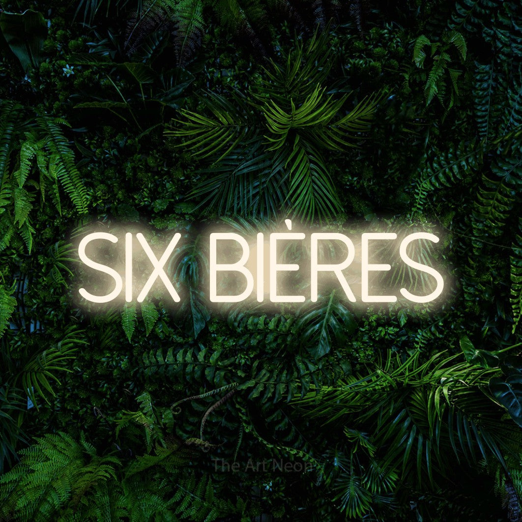 “Six bières” LED neon sign in warm white, with thin sans-serif lettering, shown against dense tropical foliage.