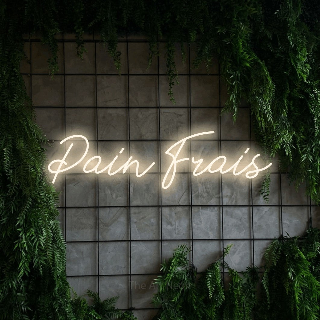 “Pain frais” LED neon sign in warm white, with cursive lettering, shown against an ivy-covered concrete grid.