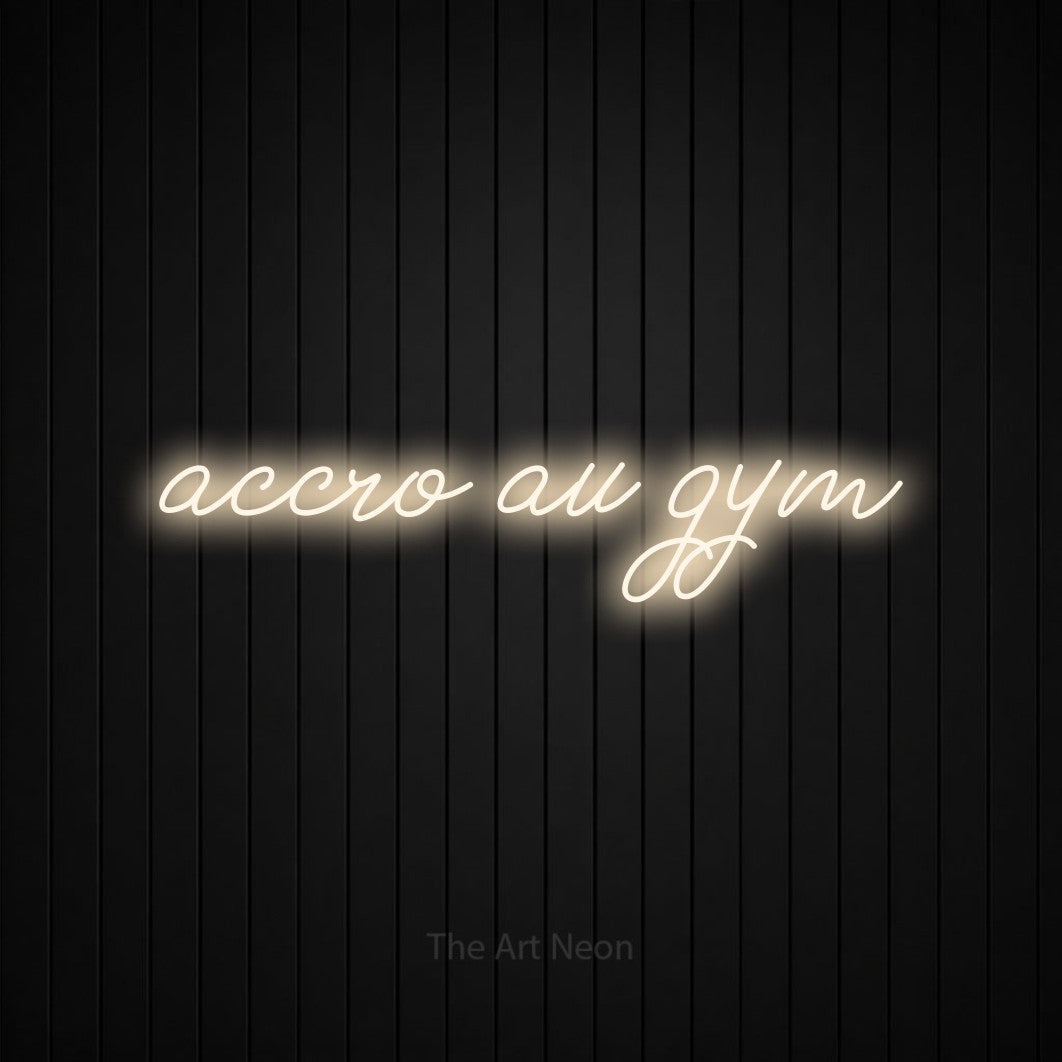 “Accro au gym” LED neon sign in warm white, with cursive lettering, shown against black vertical wall slats.