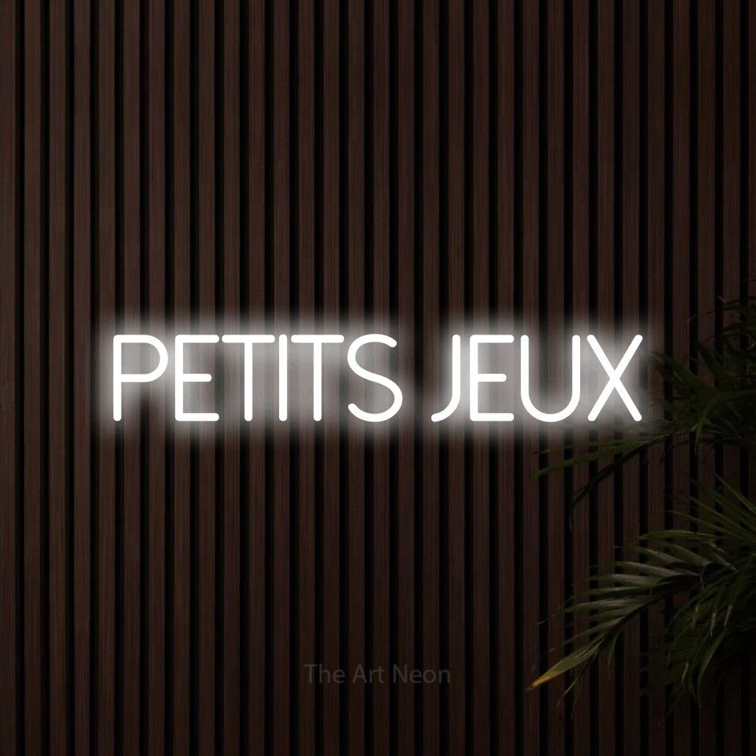 Composition en néon LED « Petits jeux » en blanc froid, en lettres fines sans empattement, mise en valeur sur un mur de lattes en bois foncé, pour un décor de hockey.