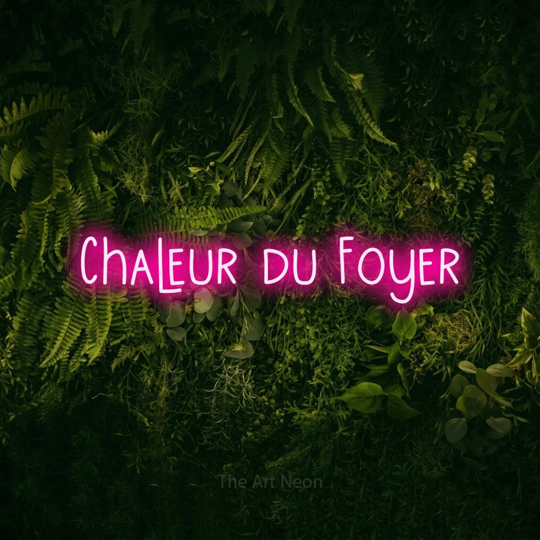 “Chaleur du foyer” LED neon sign in hot pink, with narrow hand-drawn lettering, shown against a dark moss and forest backdrop.