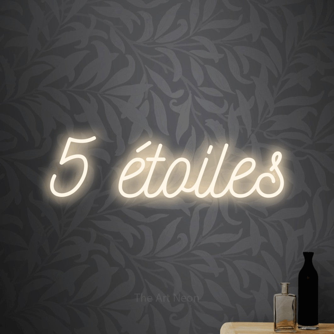 “5 étoiles” LED neon sign in warm white, with ornate cursive lettering, shown against grey botanical wallpaper.