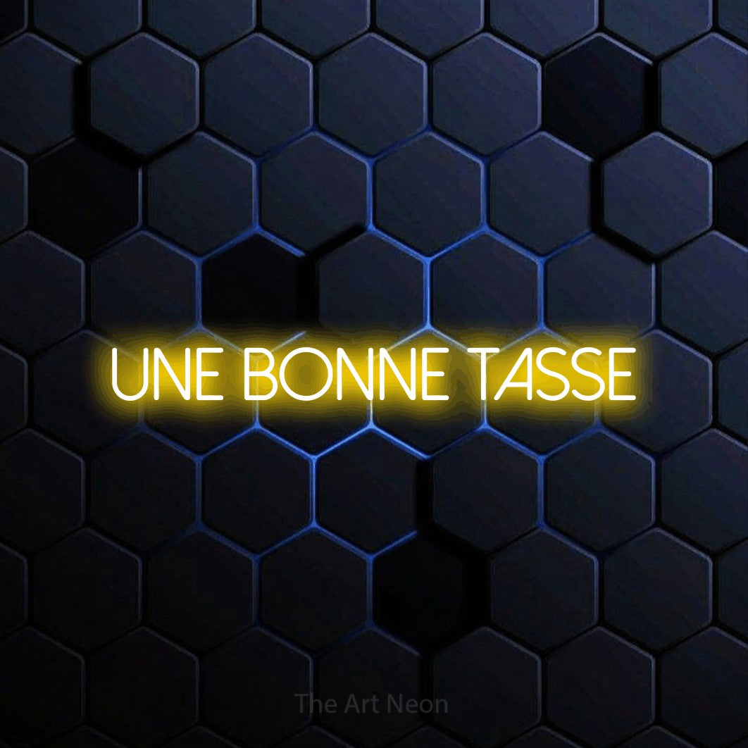 “Une bonne tasse” LED neon sign in yellow, with thin sans-serif lettering, shown against a dark blue honeycomb pattern.