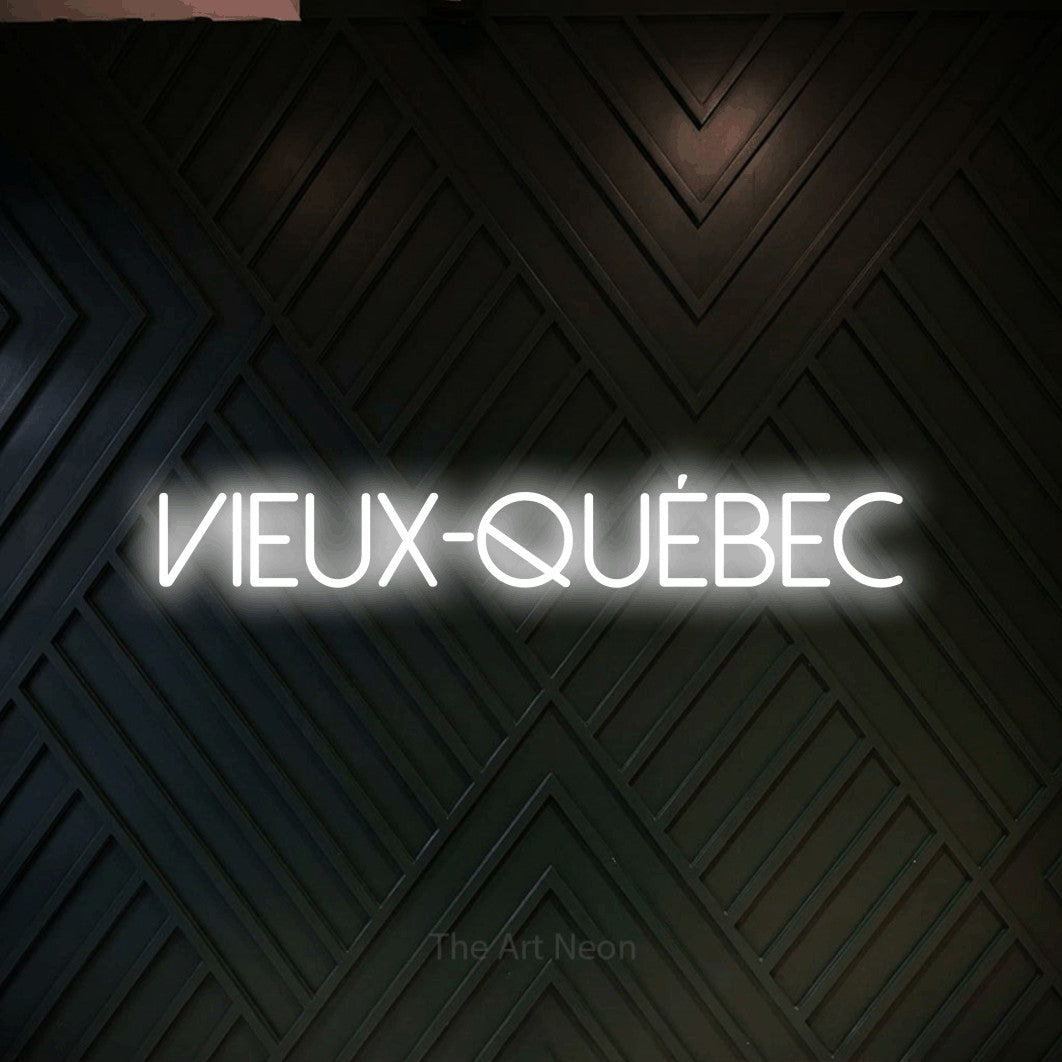 “Vieux-Québec” LED neon sign in cool white, with thin sans-serif lettering, shown against a black chevron-patterned wood wall.