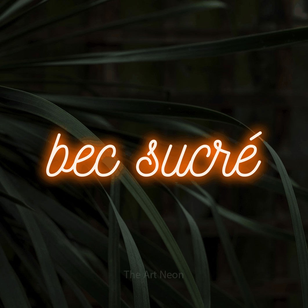 “Bec sucré” LED neon sign in orange, with ornate cursive lettering, shown against a close-up of dark foliage.