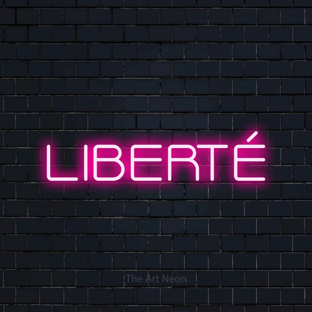 “Liberté” LED neon sign in hot pink, with rounded geometric lettering, shown against a dark navy brick wall.