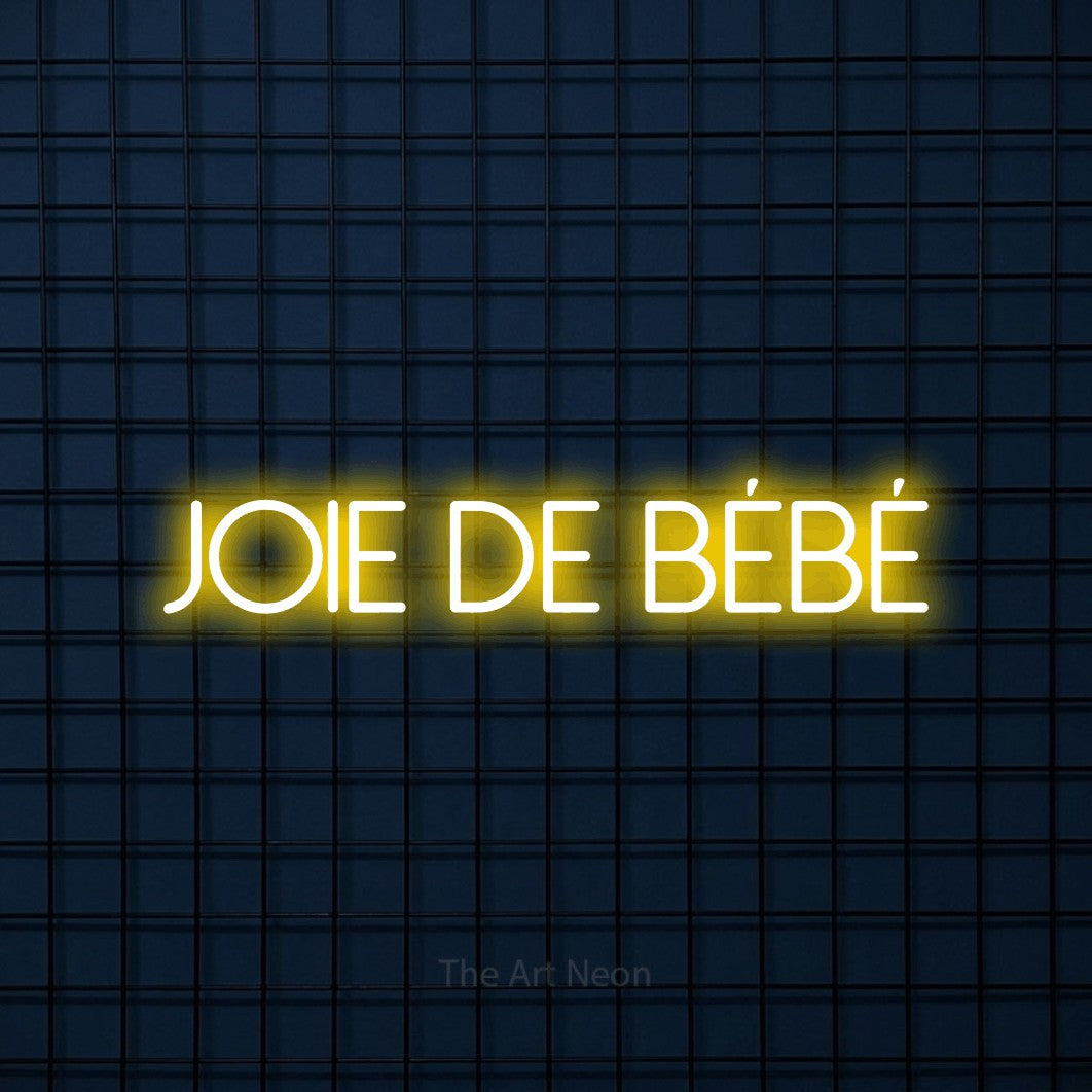 Néon LED « Joie de bébé » en jaune, en lettres fines sans empattement, mis en scène sur une grille bleu foncé, pour une fête prénatale.