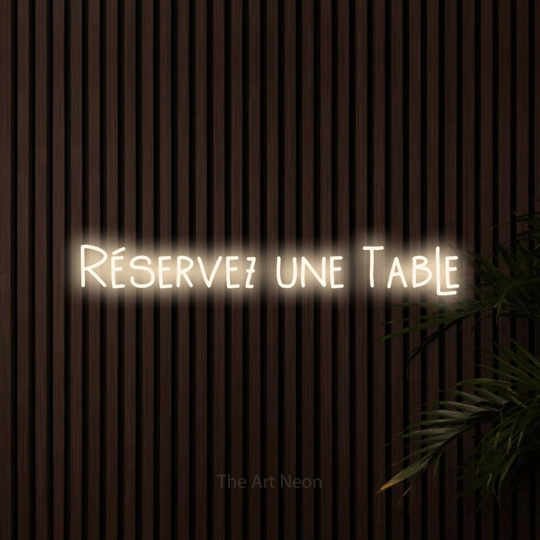 “Réservez une table” LED neon sign in warm white, with narrow hand-drawn lettering, shown against dark wooden wall slats.