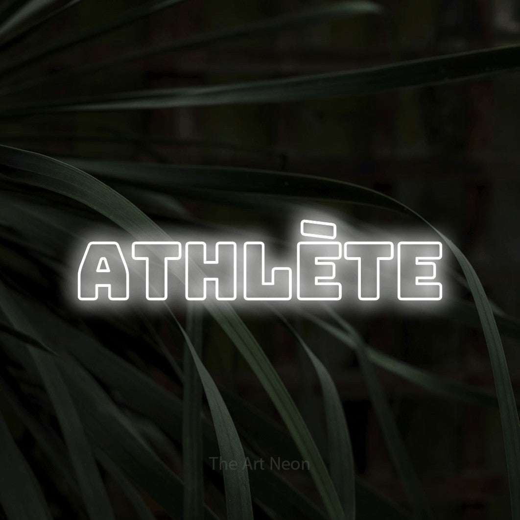 “Athlète” LED neon sign in cool white, with bold outline lettering, shown against a close-up of dark foliage.