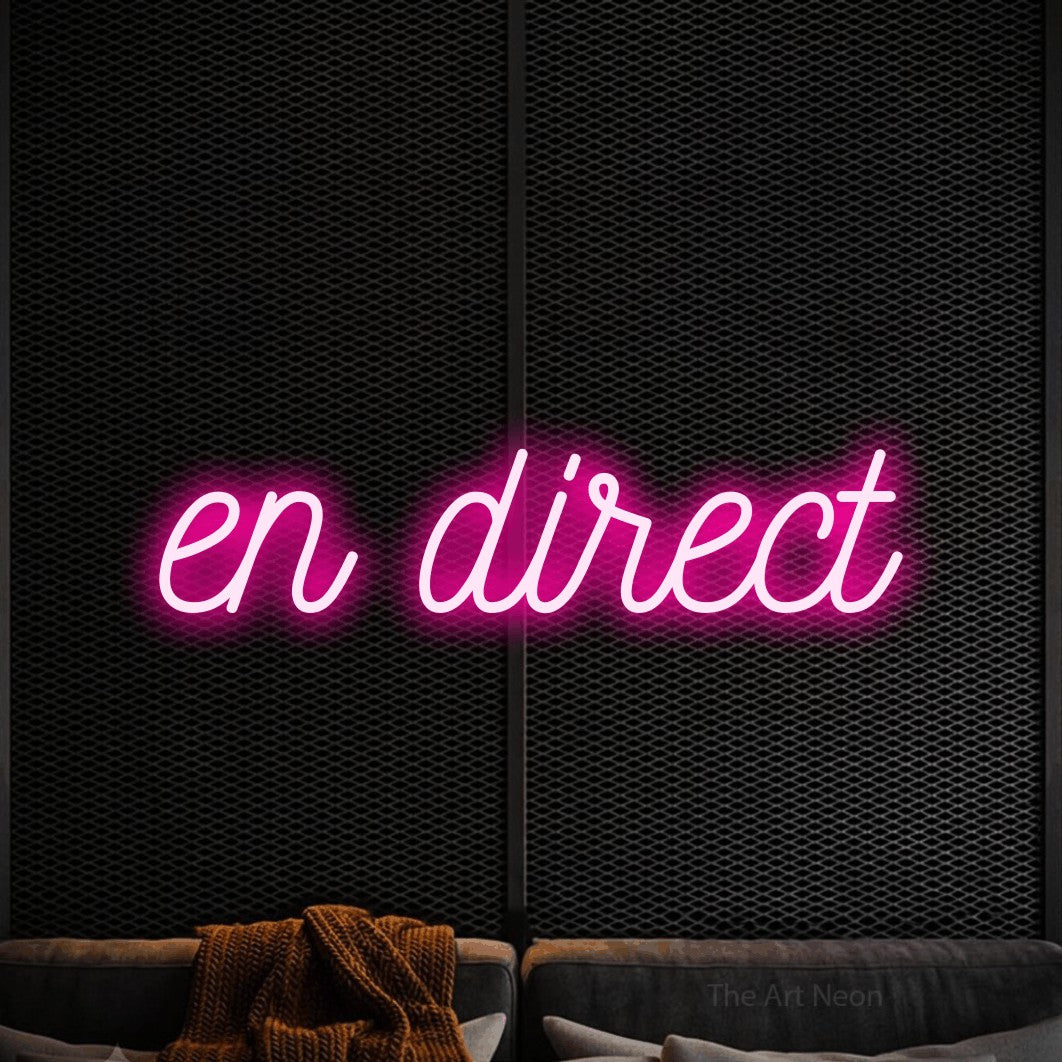 “En direct” LED neon sign in hot pink, with ornate cursive lettering, shown against a modern dark-toned seating area.