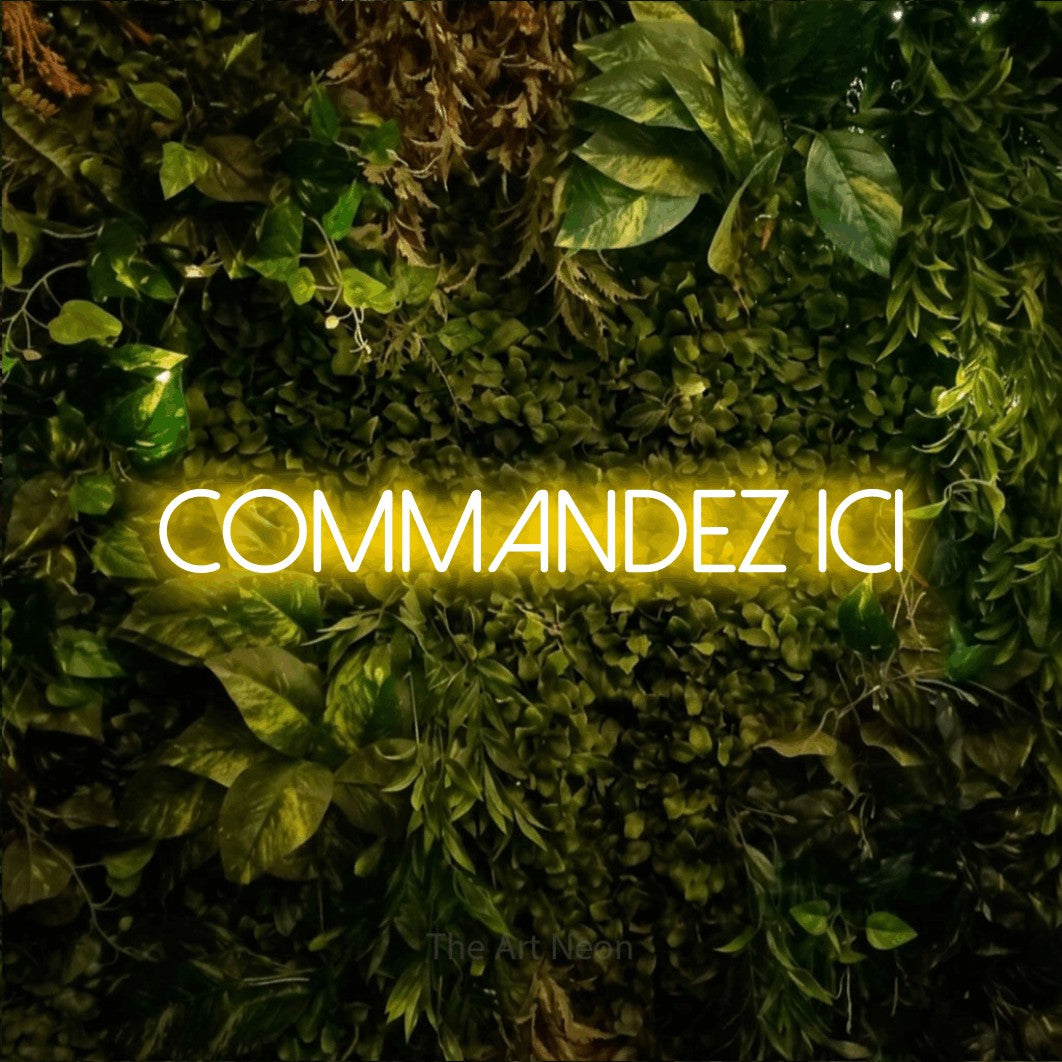 “Commandez ici” LED neon sign in yellow, with thin sans-serif lettering, shown against bright green and yellow foliage.