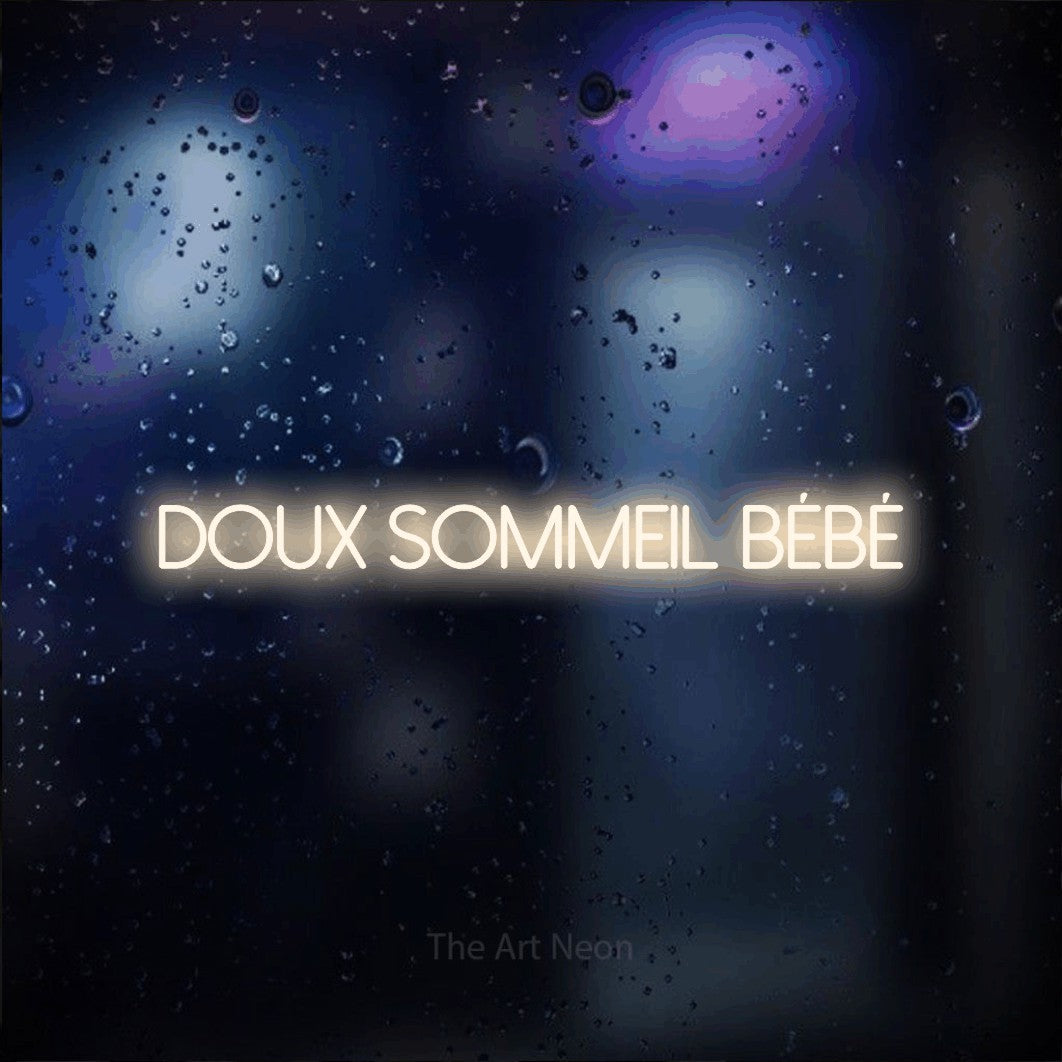 Composition en néon LED « Doux sommeil bébé » en blanc chaud, en lettres fines sans empattement, mise en valeur sur une vitre aux reflets bleus et violets, pour une fête prénatale.