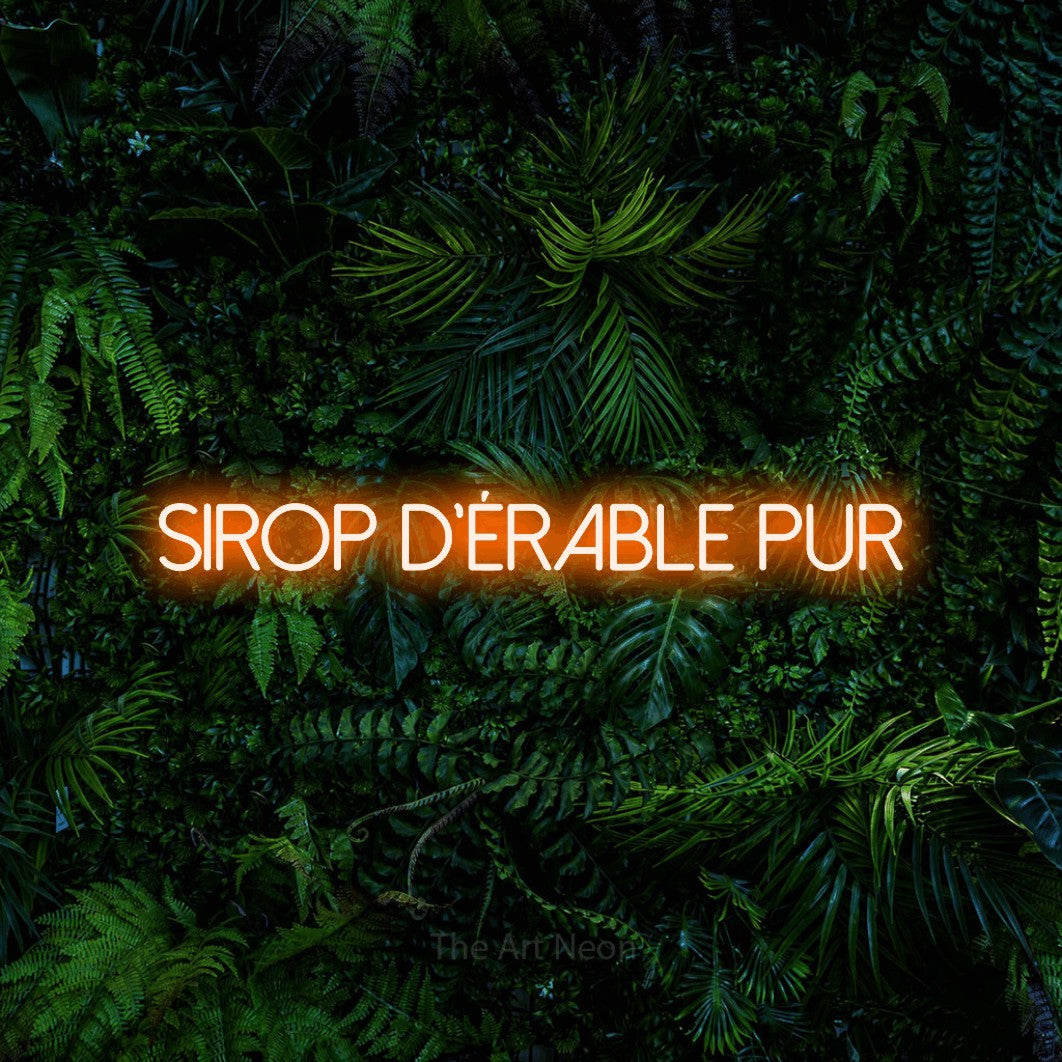 “Sirop d'érable pur” LED neon sign in orange, with thin sans-serif lettering, shown against dense tropical foliage.