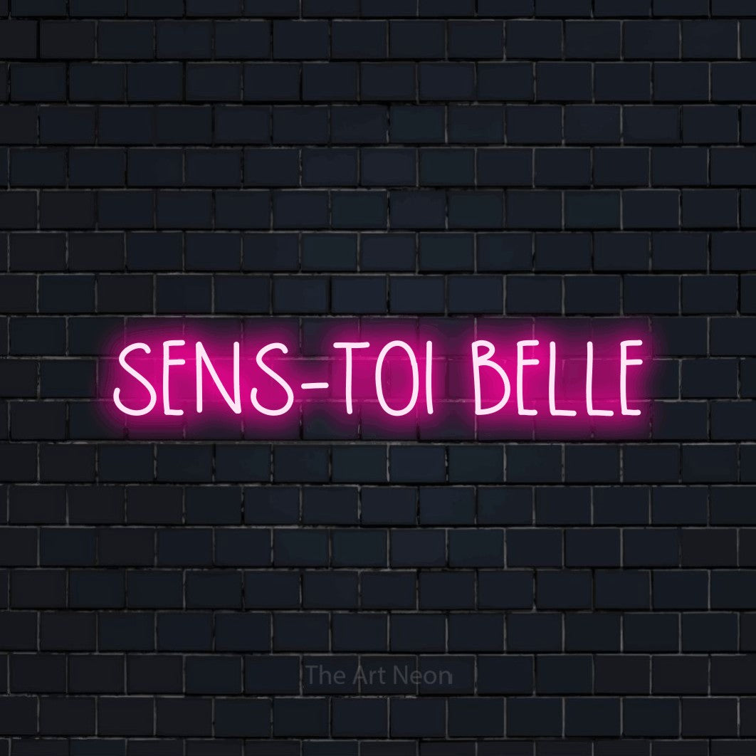 Décoration murale en néon LED « Sens-toi belle » en rose vif, en lettres étroites dessinées à la main, installée sur un mur de briques bleu marine foncé, pour un salon de beauté.