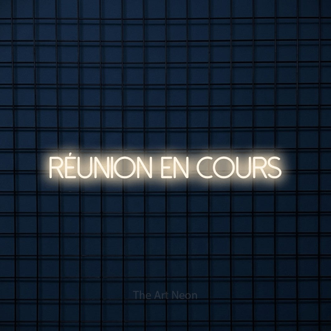 “Réunion en cours” LED neon sign in warm white, with thin sans-serif lettering, shown against a dark blue grid.