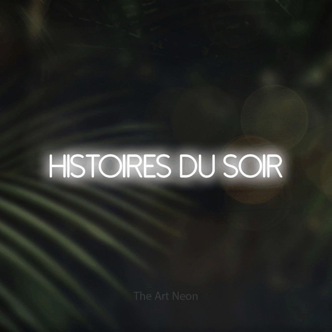 “Histoires du soir” LED neon sign in cool white, with thin sans-serif lettering, shown against a blurred palm and bokeh-light backdrop.