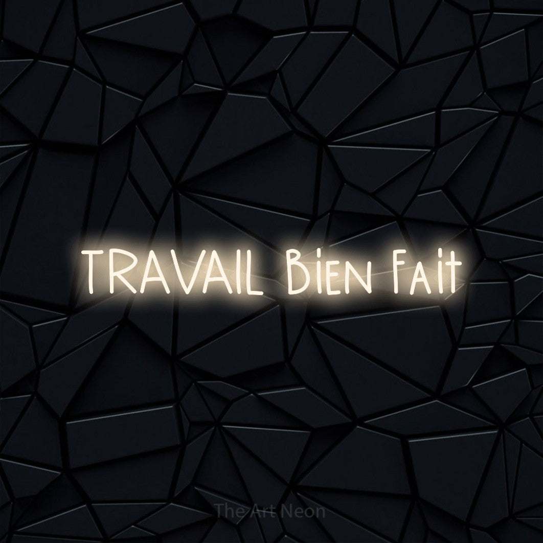 “Travail bien fait” LED neon sign in warm white, with narrow hand-drawn lettering, shown against a black polygonal surface.