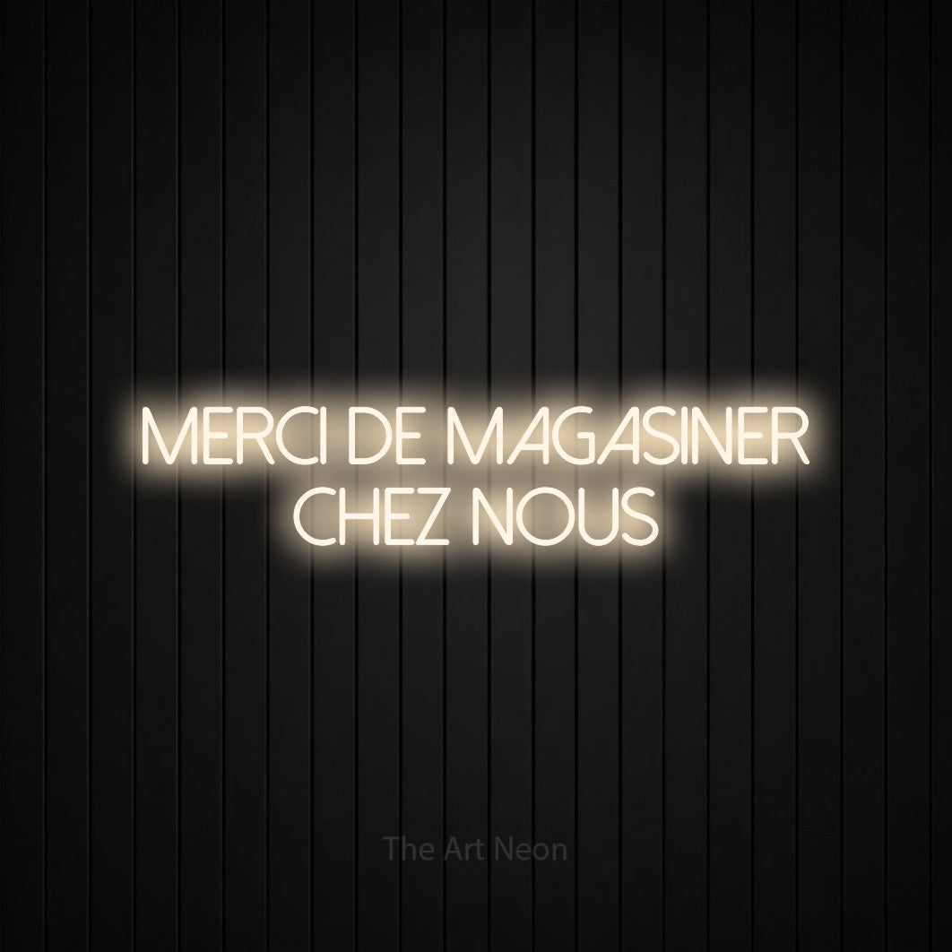“Merci de magasiner chez nous” LED neon sign in warm white, with thin sans-serif lettering across 2 lines, shown against black vertical wall slats.