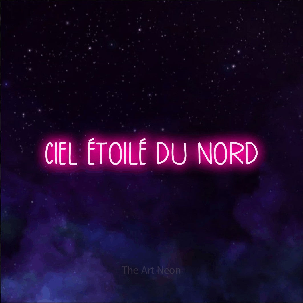 “Ciel étoilé du nord” LED neon sign in hot pink, with narrow hand-drawn lettering, shown against a purple galaxy backdrop.