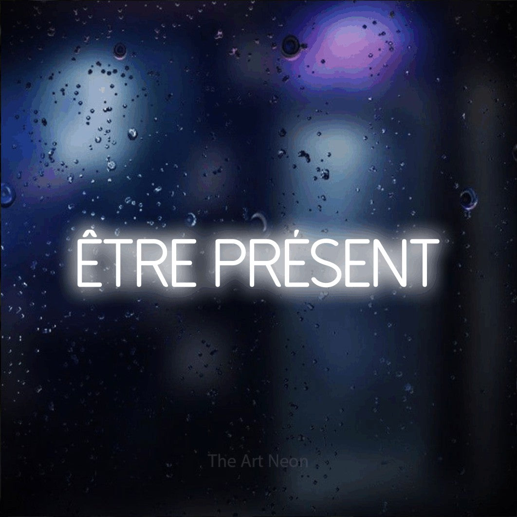“Être présent” LED neon sign in cool white, with thin sans-serif lettering, shown against glass with blue and purple reflections.