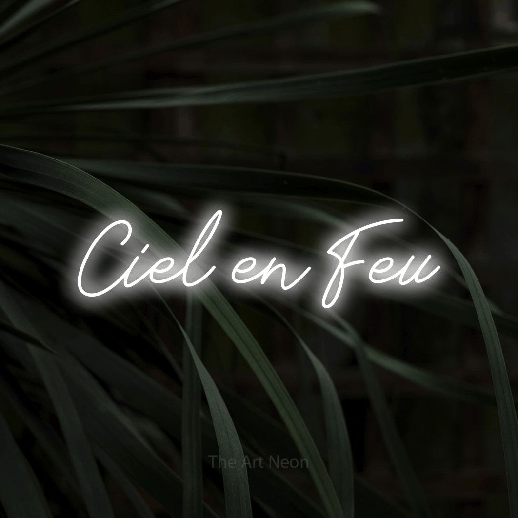 Néon LED « Ciel en feu » en blanc froid, en lettrage cursif, mis en scène sur un feuillage sombre en gros plan, pour un décor de plein air canadien.