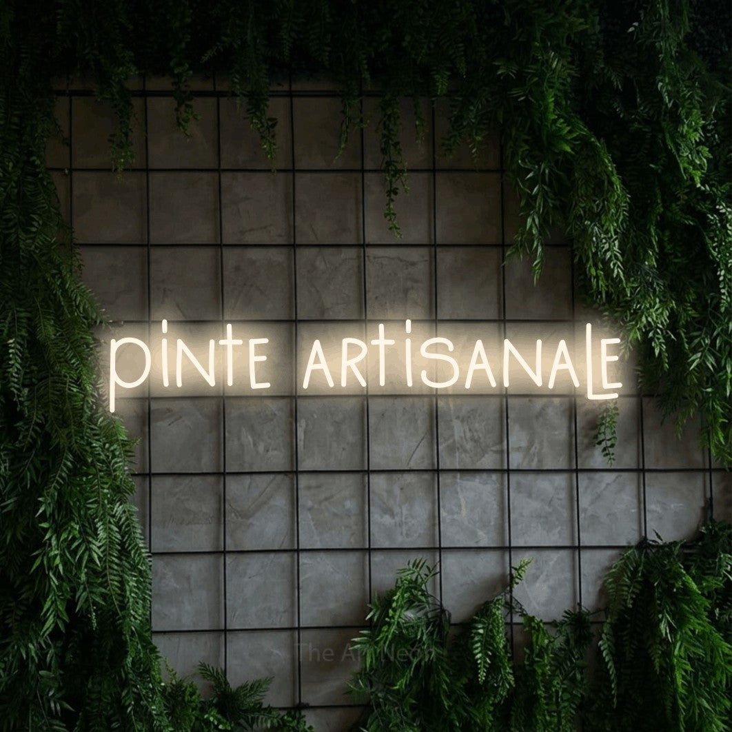 “Pinte artisanale” LED neon sign in warm white, with narrow hand-drawn lettering, shown against an ivy-covered concrete grid.