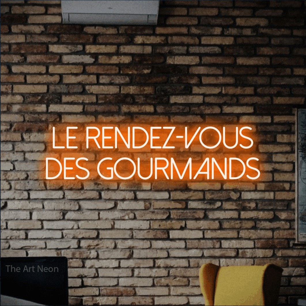 “Le rendez-vous des gourmands” LED neon sign in orange, with thin sans-serif lettering across 2 lines, shown against warm-toned brickwork.