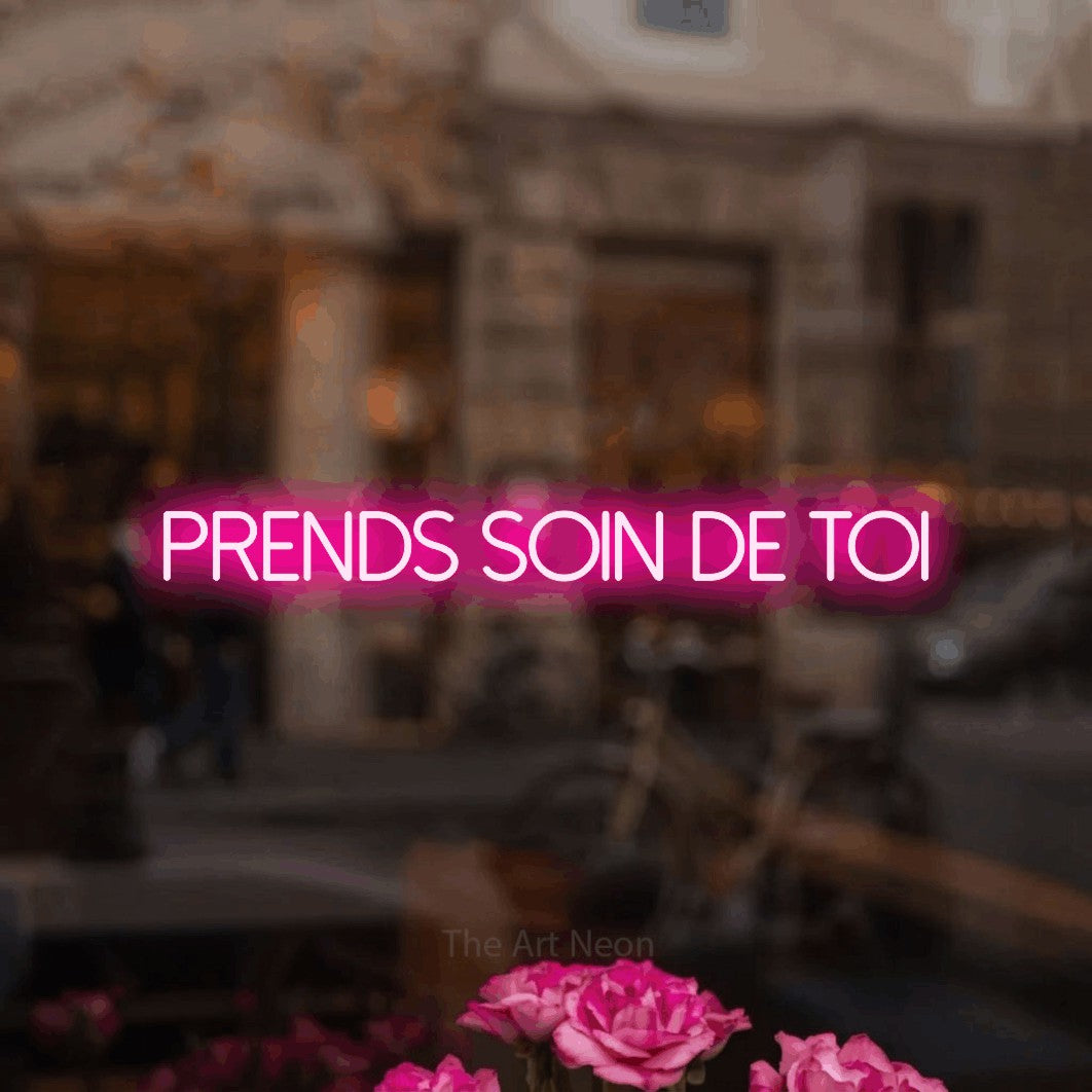 Lettrage en néon LED « Prends soin de toi » en rose vif, en lettres fines sans empattement, présenté dans un décor flou de café-bar, pour un salon de beauté.