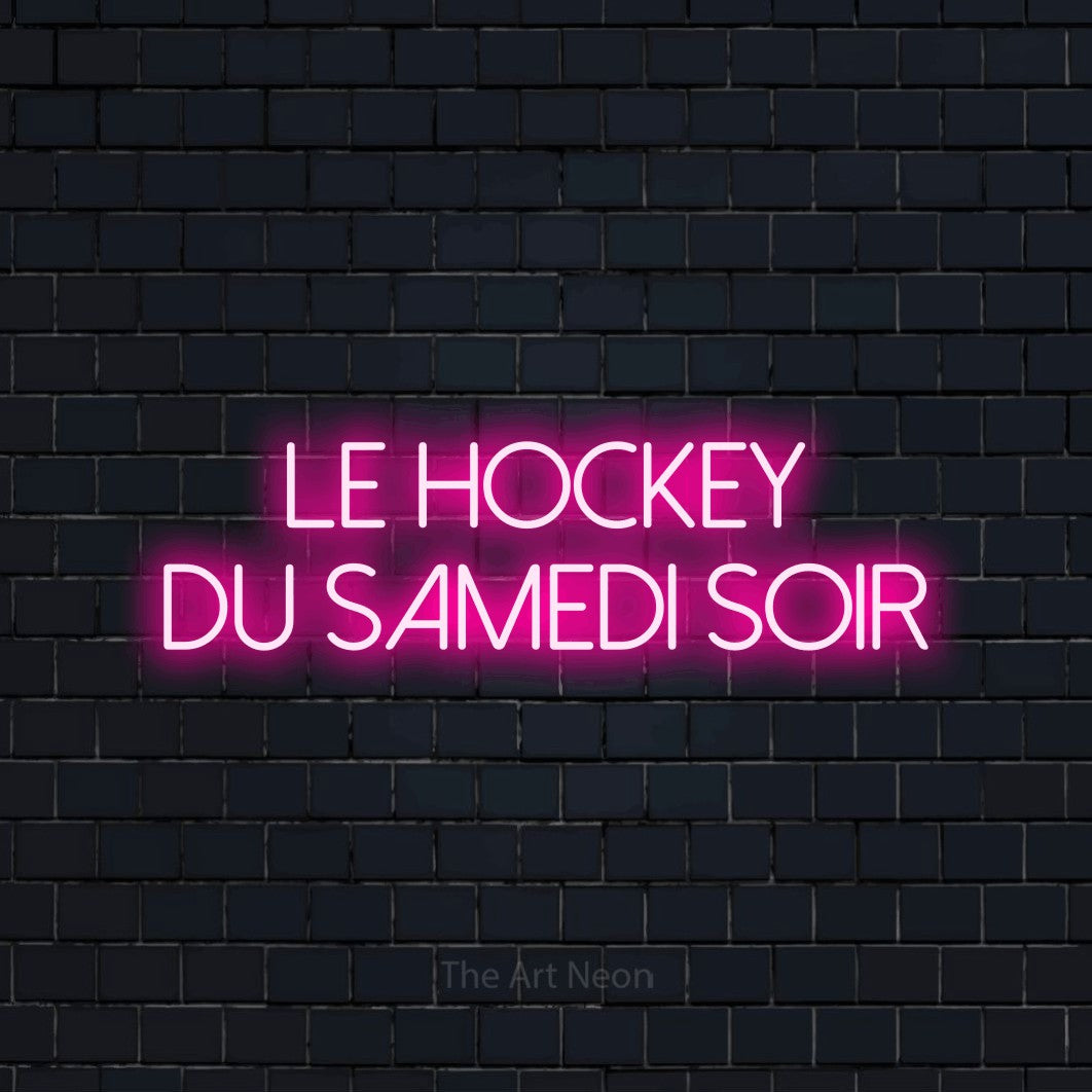 Décoration murale en néon LED « Le hockey du samedi soir » sur deux lignes en rose vif, en lettres fines sans empattement, installée sur un mur de briques bleu marine foncé, pour un décor de hockey.
